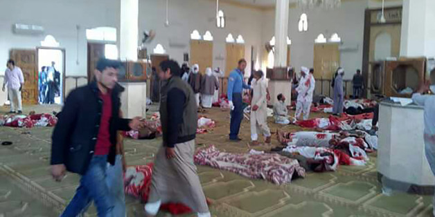 Egyptians walk past bodies following a gun and bombing attack at the Rawda mosque, roughly 40 kilometres west of the North Sinai capital of El-Arish, on November 24, 2017.A bomb explosion ripped through the mosque before gunmen opened fire on the worshippers gathered for weekly Friday prayers, officials said. / AFP PHOTO / STRINGER (Photo credit should read STRINGER/AFP/Getty Images)