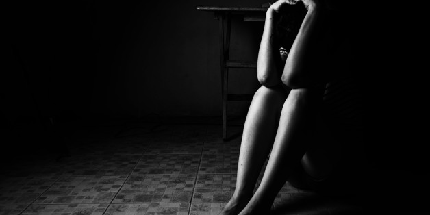 a woman sitting on ground with arm around lower head, sexual violence , sexual abuse, human trafficking concept with shadow edge in white tone