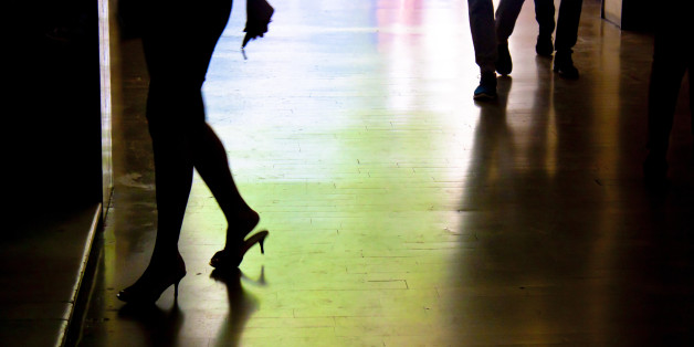 Blurry silhouette and shadow of a woman entering the building and two men behind her, from waist down, in the alley in the night in city centre