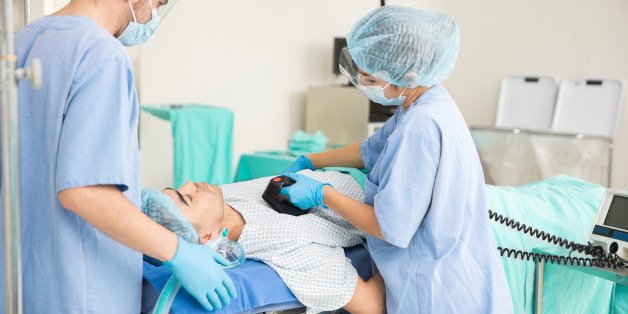 Rear view of a couple of doctors doing a cardiopulmonary resuscitation with a defibrillator
