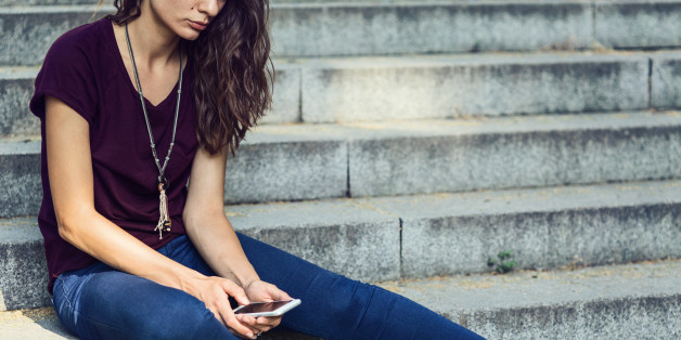Sad girl looking at the telephone and sitting on stairs outside. Creative crop â no face