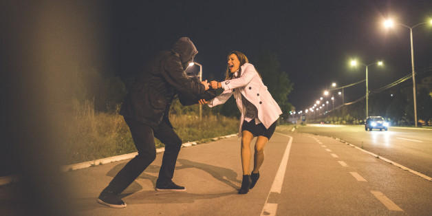 Robber stealing businesswomans bag on the middle of the street at night.