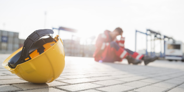 Yellow hardhat at shipyard with depressed male worker in background