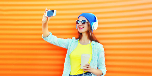 Fashion pretty cool girl makes self portrait on smartphone over colorful orange background