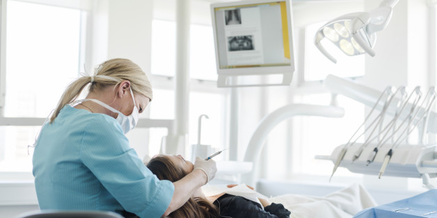 Female dentist checking patient. Woman is sitting on dentist's chair. They are in brightly lit dental clinic.