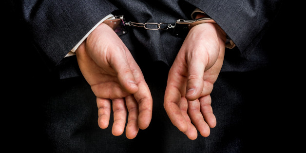 Arrested businessman in handcuffs with hands behind back - isolated on black background