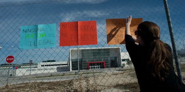 A woman hangs placards reading 'Nobody is illegal' and 'No flags no borders' outside the new and yet to open jail of Archidona, on November 26, 2017, where nearly 500 migrants who arrived in the country by boat last week are held.The Spanish government said that the migrants are held in Archidona´s jail due to a lack of space at immigration detention centres. Migrants who arrive in Spain by boat are usually initially detained in police facilities for identification and processing before being