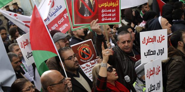 Palestinian protesters hold placards as the convoy of Jerusalem's Greek Orthodox patriarch Theophilos III arrives in the West Bank town of Bethlehem on January 6, 2018 ahead of a Christmas service according to the Eastern Orthodox calendar. The municipalities of Bethlehem, Beit Sahour and Beit Jala, all in the Israeli-occupied West Bank, called for the boycott over Jerusalem's Greek Orthodox patriarch allegedly allowing controversial real estate sales. / AFP PHOTO / Musa AL SHAER (Photo