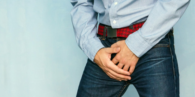The guy in the jeans and blue shirt holding hands his crotch on the blue background. Incontinence. Disease for men. Men's health. The pain from the blow in groin.