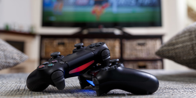 Playing video game. Console controllers or joysticks. Football or soccer game on the television. Widescreen tv stands on commode.