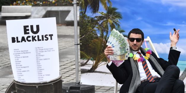 An Oxfam activist stages a satirical street-play mimicking a wealthy person hidding his money in a tax haven, on December 5, 2017 near the European institutions in Brussels, within a meeting of European Union ministers over a credible blacklist of non-EU tax havens. The EU has struggled for over a year to finalise the blacklist, with smaller, low-tax EU nations such as Ireland, Malta and Luxembourg worried about scaring off multinationals. / AFP PHOTO / EMMANUEL DUNAND (Photo credit shoul