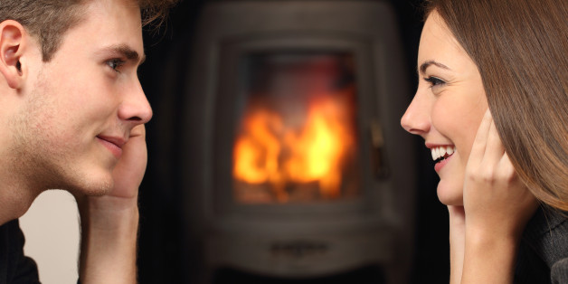 Side view of a couple flirting and looking each other in front a fireplace