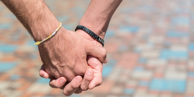 Close up on the clasped hands of a gay couple.