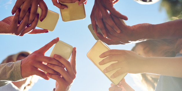 Cropped shot of a group of friends using their phones together outdoors