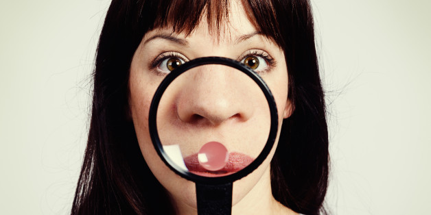 A young brunette beauty looks shocked as she examines her nose through a magnifying glass, discovering freckles or - worse - blackheads!