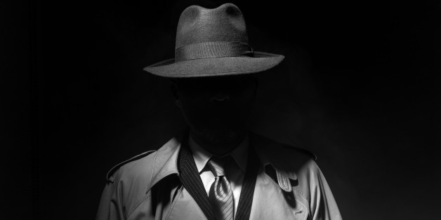 Man posing in the dark with a fedora hat and a trench coat, 1950s noir film style character