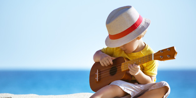 Little boy plays on Hawaiian guitar or ukulele at sea beach background. Space for text