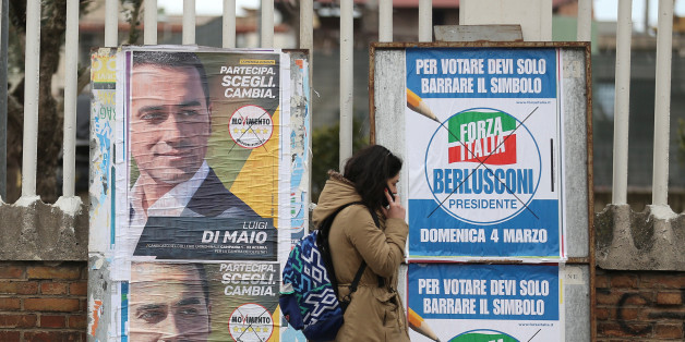 A woman walks past electoral posters of the 5 Star's candidate Luigi Di Maio and the Forza Italia party in Pomigliano D'Arco, near Naples, Italy, February 21, 2018. Picture taken February 21, 2018. REUTERS/Alessandro Bianchi