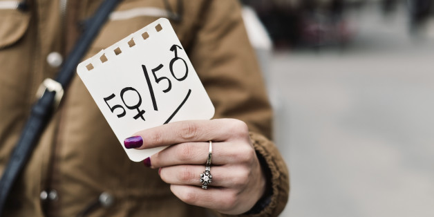 young caucasian woman in the street shows a paper with the text 50/50 written in it, with the zeros as the female and male gender symbols, depicting the gender parity concept, negative space on right