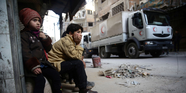 Des enfants regardent passer un convoi d'aide humanitaire du Croissant Rouge syrien dans la ville assiégée de Douma, Ghouta orientale, Damas, Syrie, le 5 mars 2018.